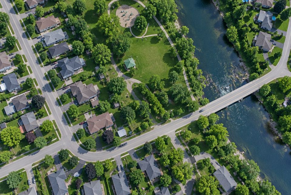 A view from above of houses, roads, a park and a river crossed by a bridge.