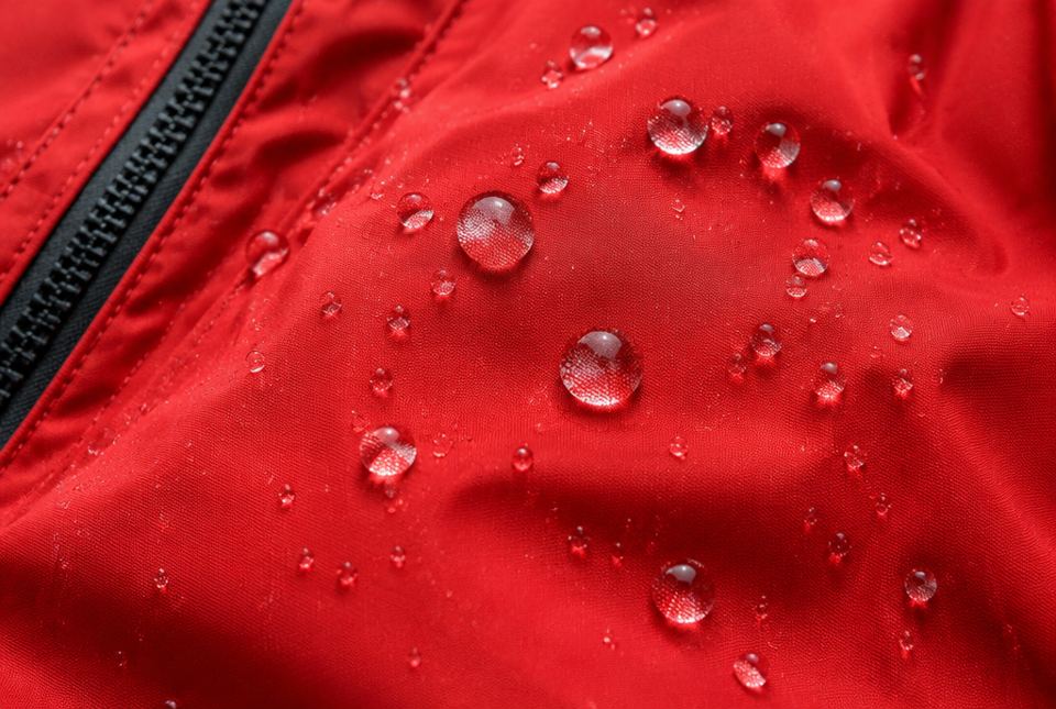 Round water drops sitting on the fabric of a red rain jacket.