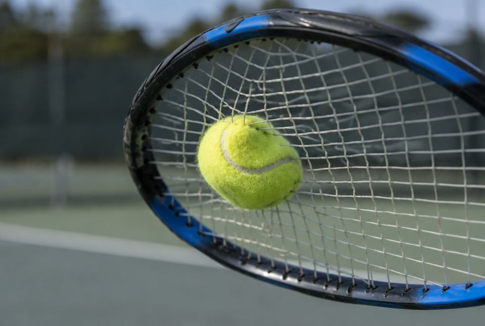 A tennis ball hitting the strings of a tennis racket on an outdoor court.