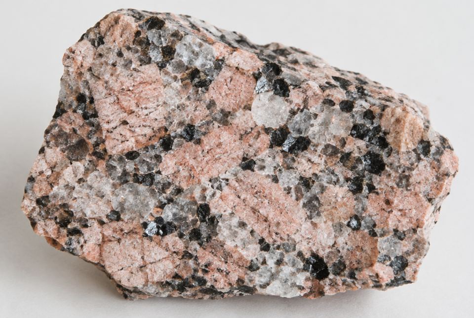 A close-up of a piece of granite showing pink, glassy grey-white and black mineral grains.