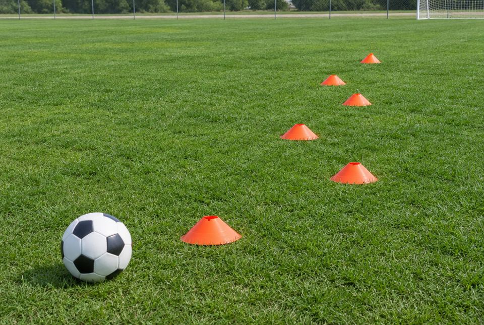 A soccer ball on a grass field next to a zig-zag line of orange cones.