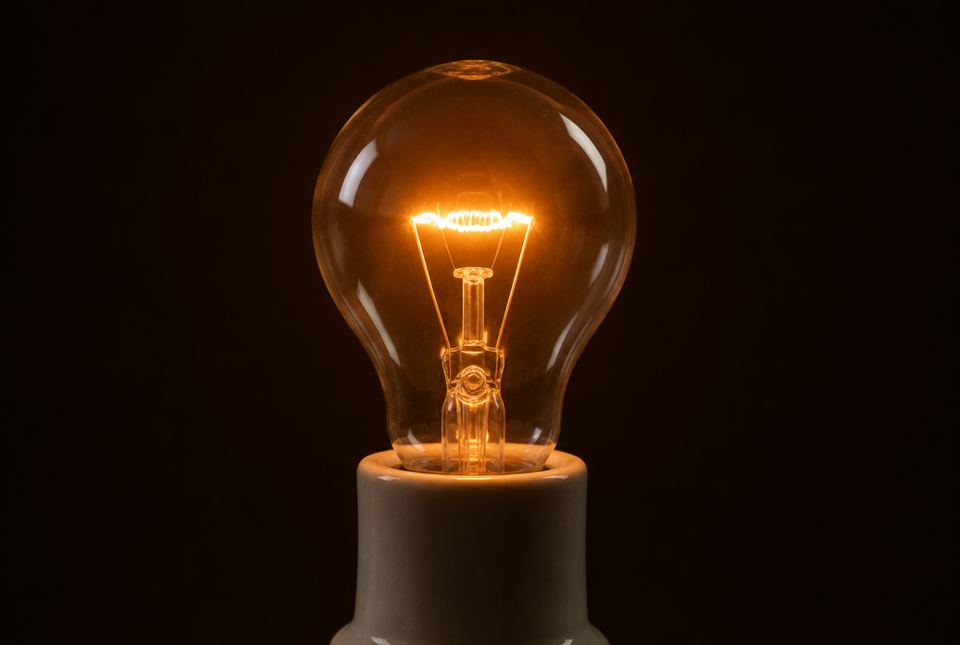 A clear old-style light bulb with its coiled filament glowing orange.