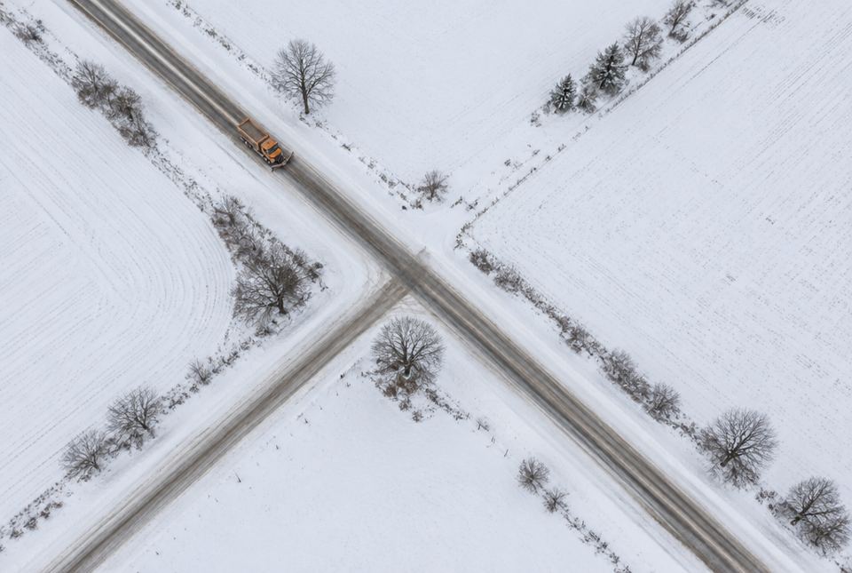 An aerial view of two snowy country roads crossing in an X, with a snowplough on one road.