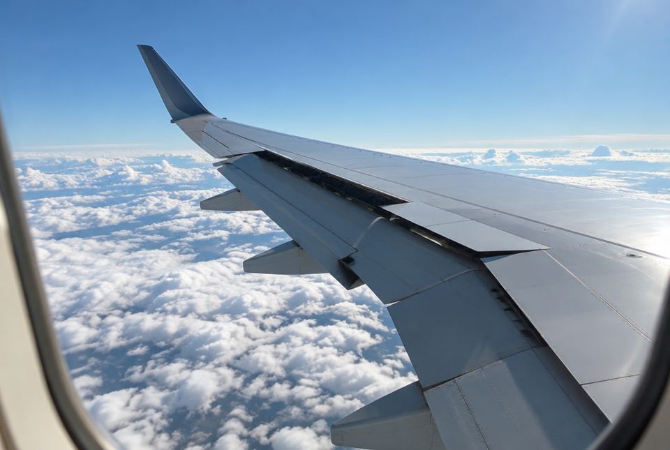 A view out an airplane window of the wing over a sea of white clouds.