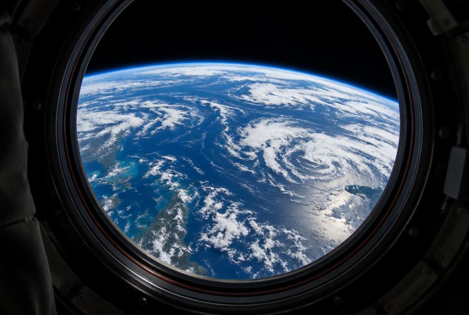 Planet Earth, with blue oceans and swirling white clouds, seen through the round window of a spacecraft.