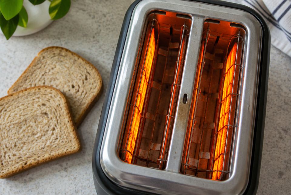 Looking down into a toaster whose heating wires glow bright orange, with two slices of bread beside it.