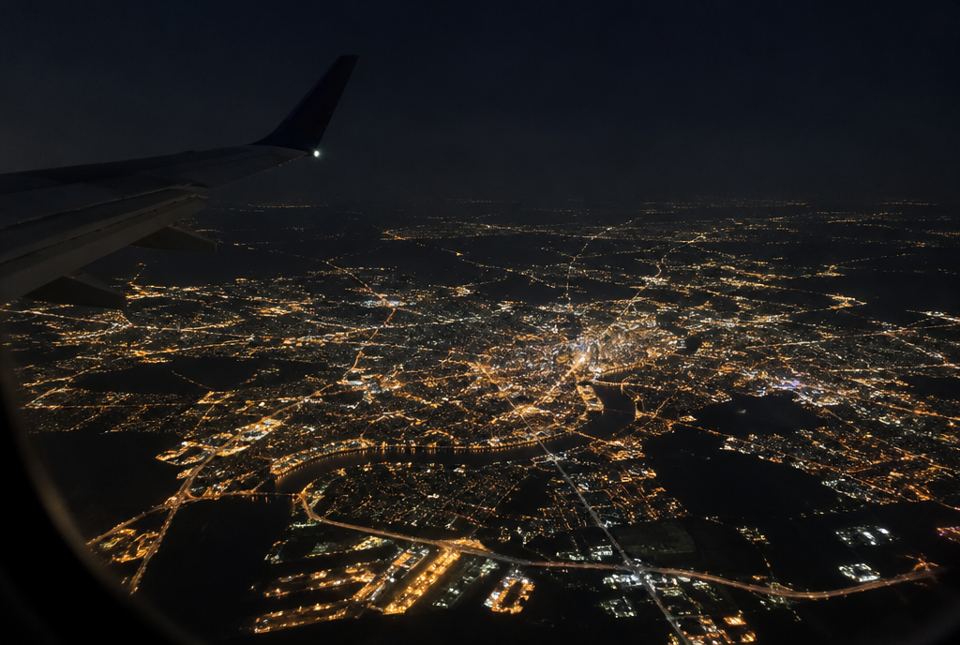 A large city glowing with lights at night, seen from an airplane window.