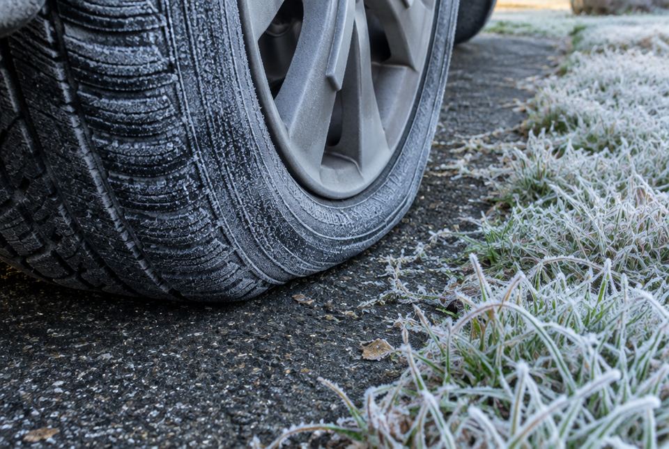 A car tire on a frosty morning, with frost on the tire and on the grass beside it.